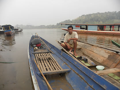 photo of a man sitting in a wooden boat, a river and other similar boats