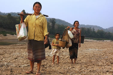 photo of women and a small child carrying burdens near a river