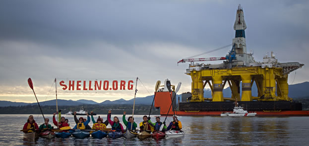 photo of kayakers near an oil platform holding a sign that reads shellnoorg