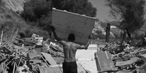 photo of a man carrying a sheet of plywood out of a pile of like objects