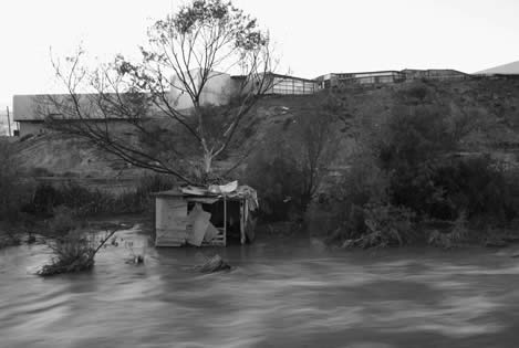 photo of a shack built at the waterline of a creek, gleaming offices above the bank