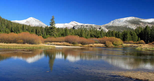 photo of a river flowing in a meadow under snowy peaks