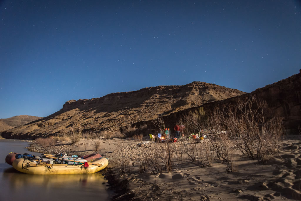 photo of a raft pulled up to an inviting sandbar on a desert river under an evening sky