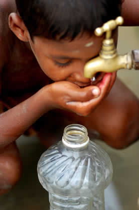 photo of a child drinking from a faucet, worn plastic bottle in foreground