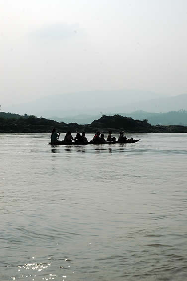 photo of an open boat with several people on it being paddled over a huge expans of river, mountains in the background