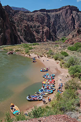 photo looking down from a height at a dozen river rafts on a canyon river beach