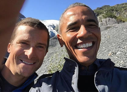 two men looking into a camera, selfie-style, in an outdoor mountain setting