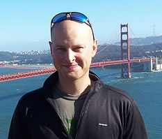 photo of a bald man standing with the Golden Gate Bridge in the background
