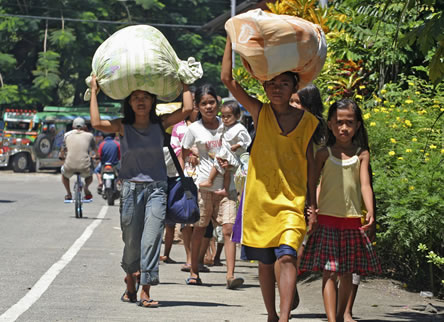 photo of people walking on an urban street carrying large bundles on their heads