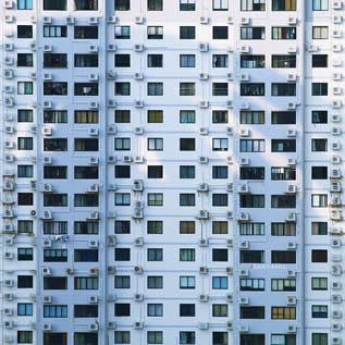 photo of the side of a tall building, windows covered with AC units