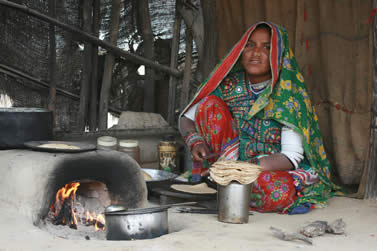 photo of a woman in multicolored clothing using an oven to cook flatbread