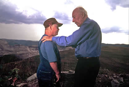 photo of two men on the scene of a coal mine; one in overalls and another older man speaking to him seriously