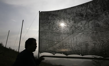 photo of a person in silhouette, fabric net stretched across a frame nearby