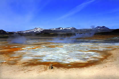 photo of a geothermal pond, steam and thermophillic algae visible
