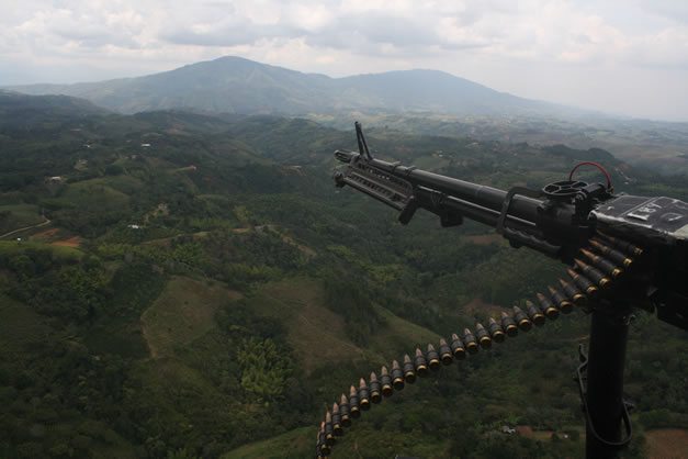 photo of a machine-gun pointed out the door of a helicopter, flying over a misty forested landscape