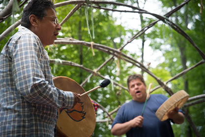 photo of two men playing handmade drums and singing in a forest