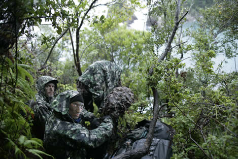 photo of men in full camouflage, in a rainy thicket of greenery